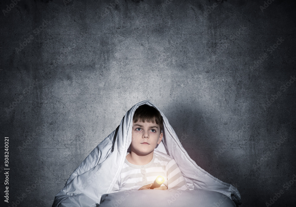 Little child with flashlight hiding under blanket