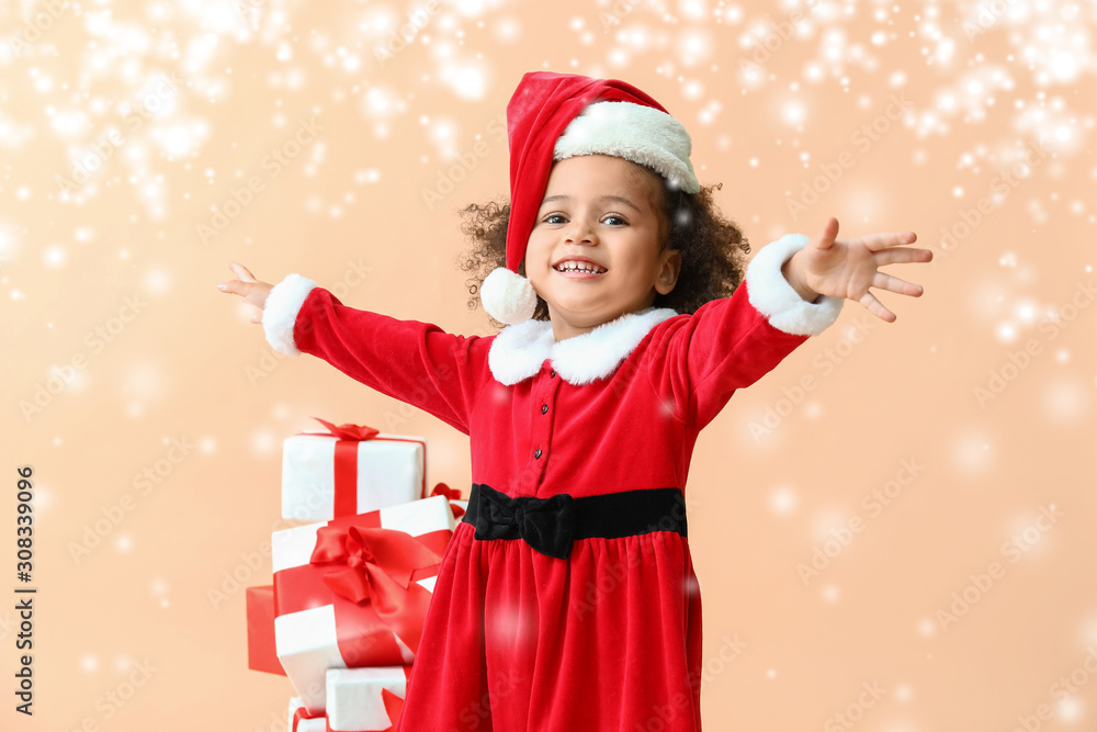 Little African-American girl in Santa costume and with gifts on color background with snow