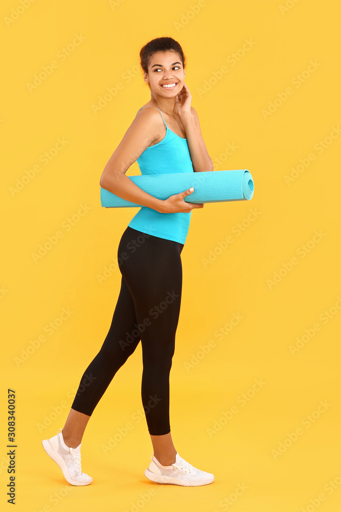 Sporty African-American woman with yoga mat on color background