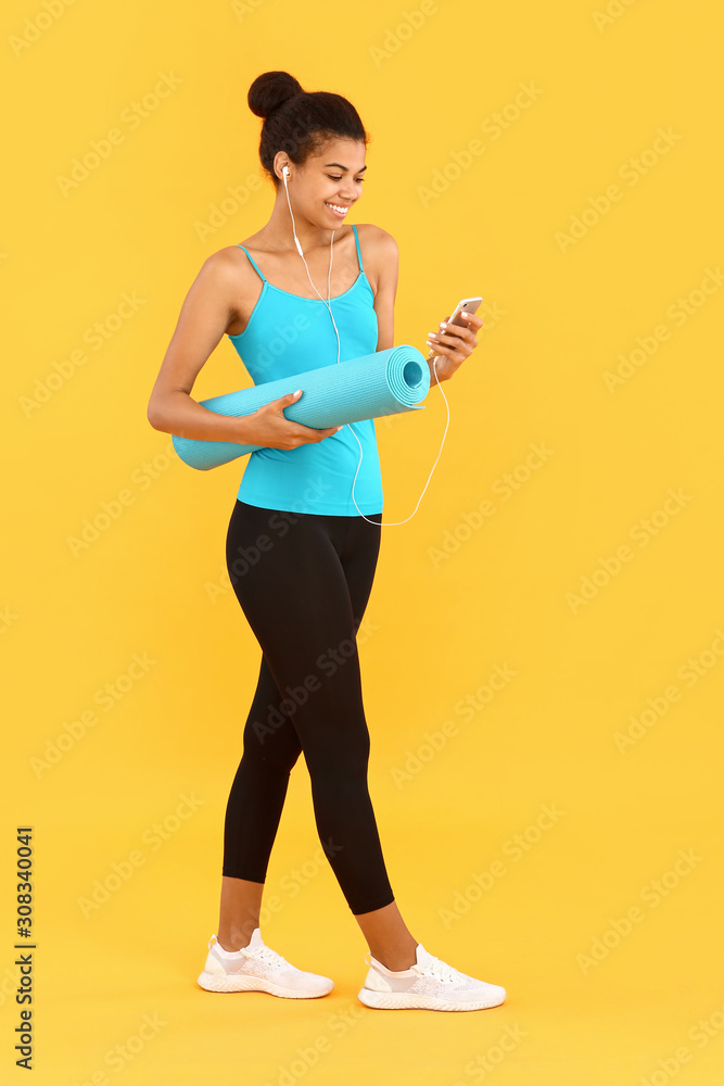 Sporty African-American woman with yoga mat and mobile phone on color background