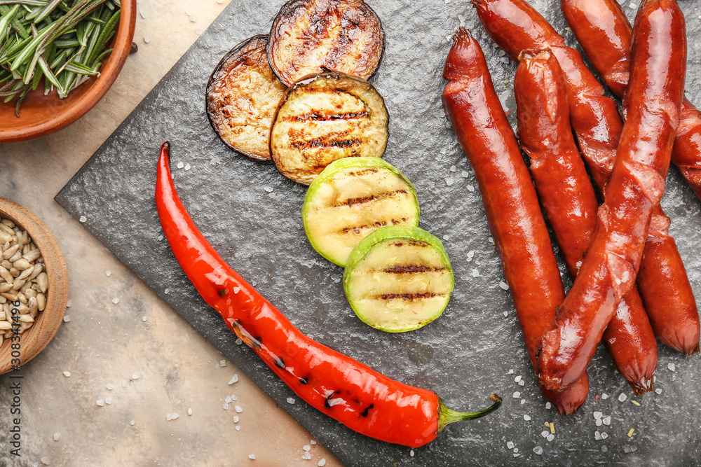 Tasty grilled sausages with vegetables on slate plate