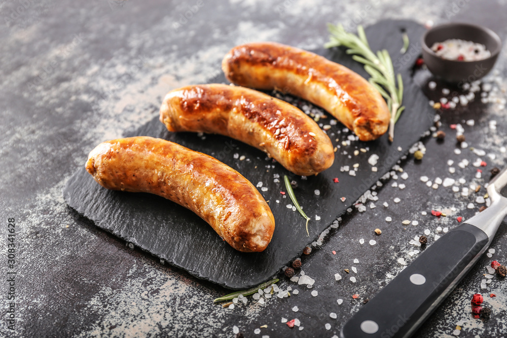 Slate plate with tasty grilled sausages with spices on dark background