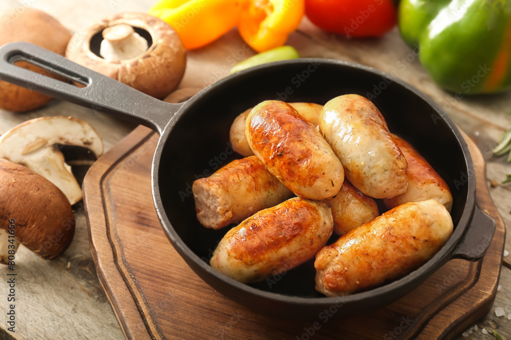 Frying pan with tasty grilled sausages on wooden table