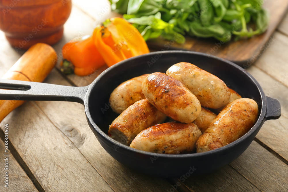 Frying pan with tasty grilled sausages on wooden table