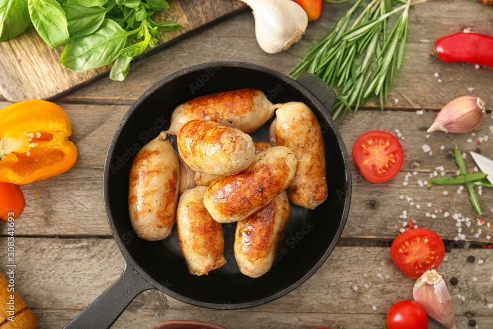 Frying pan with tasty grilled sausages on wooden table