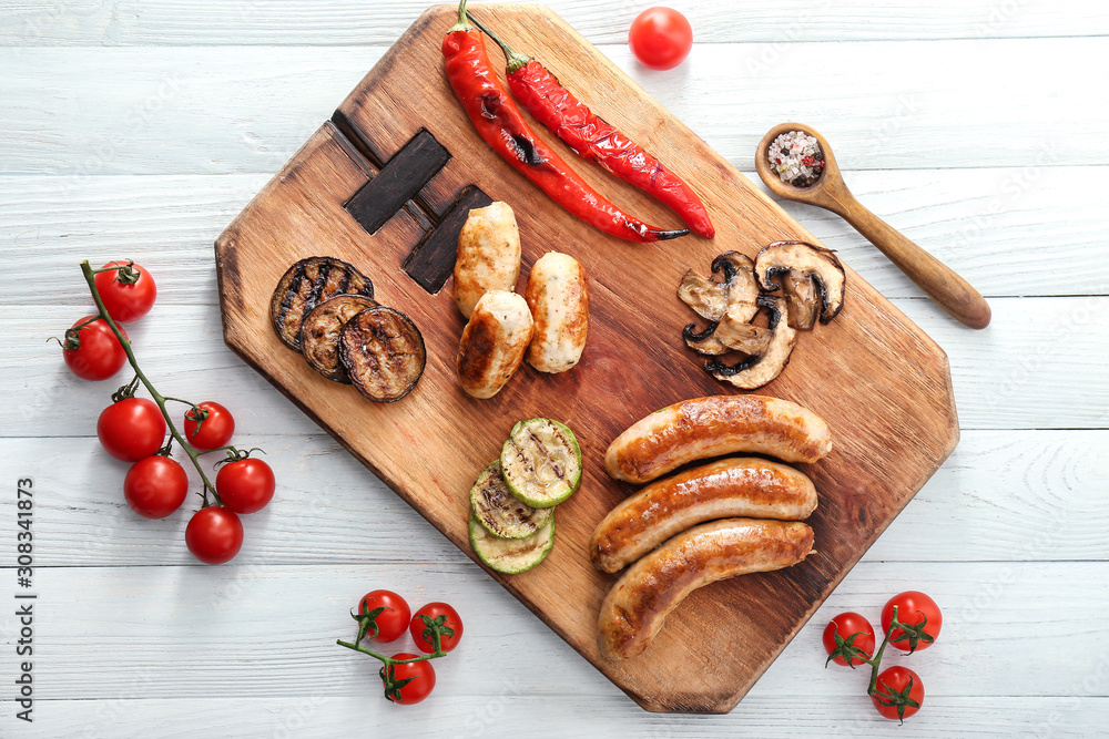 Wooden board with tasty grilled sausages and vegetables on wooden table