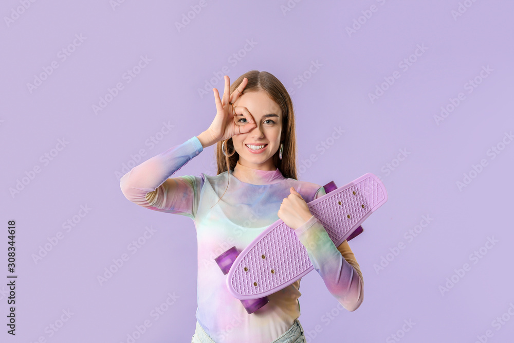 Stylish hipster girl with skateboard showing OK gesture on color background