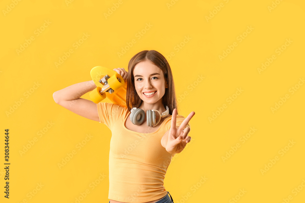 Stylish hipster girl with skateboard showing victory gesture on color background