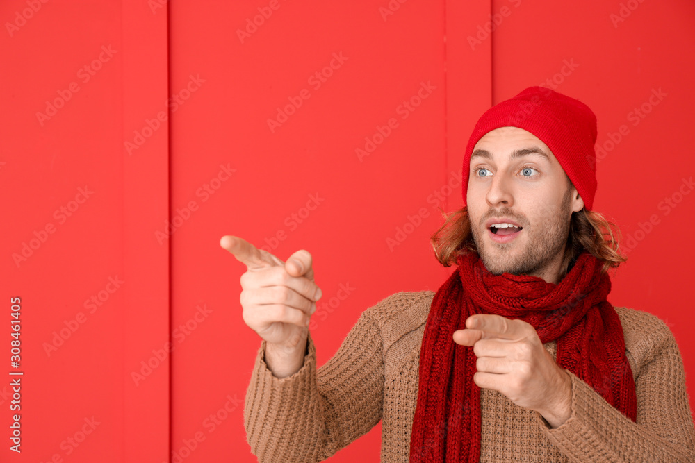 Handsome man in winter clothes pointing at something on color background