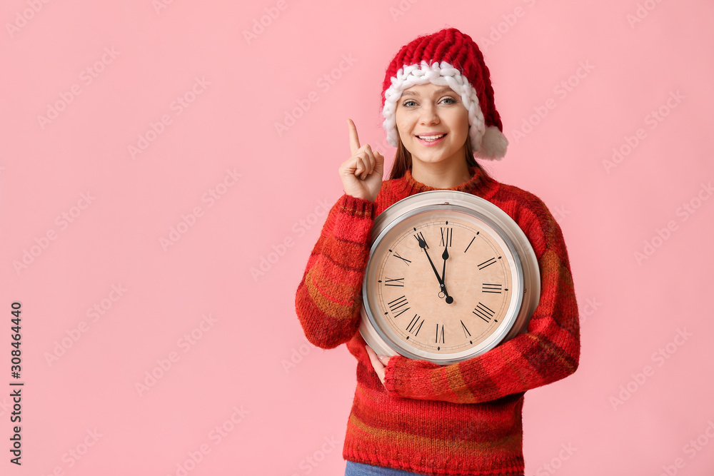 Young woman in Santa hat and with clock on color background. Christmas countdown concept