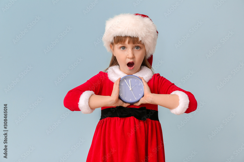 Surprised little girl in Santa costume and with alarm clock on color background. Christmas countdown