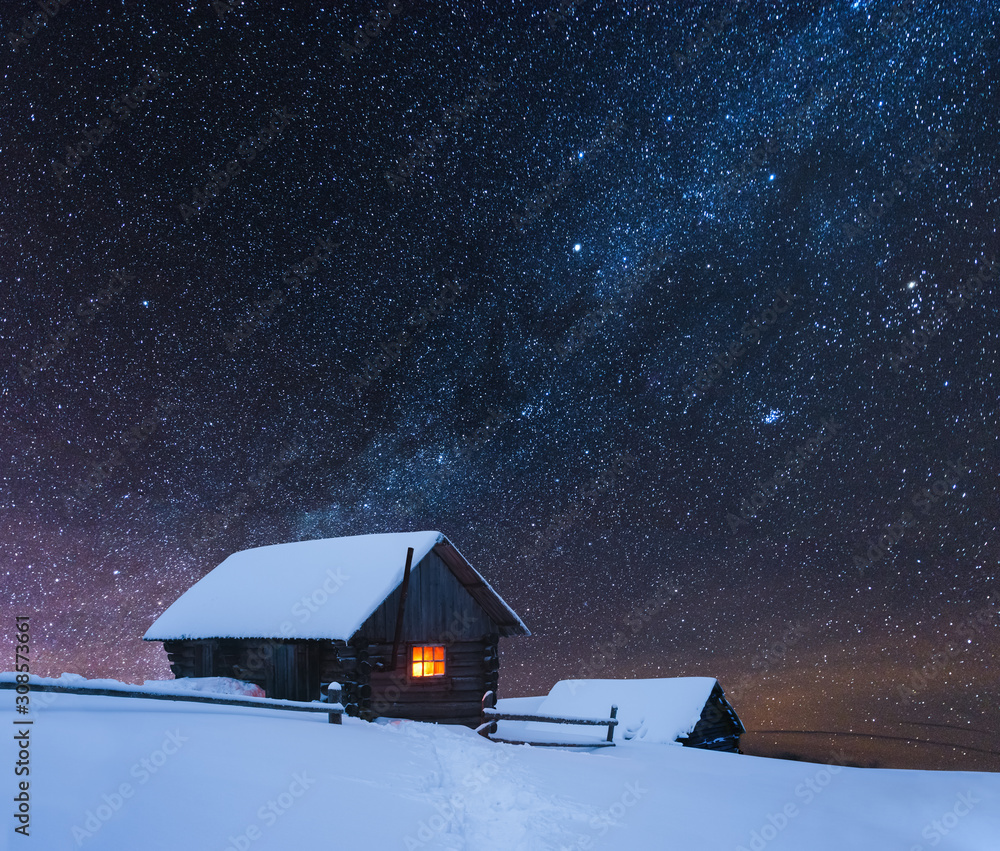 Dramatic wintry scene with snowy house with warm light in window. Fantastic night landscape glowing 