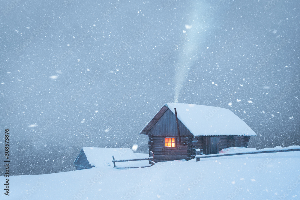 Fantastic winter landscape with wooden house in snowstorm in snowy mountains. Smoke comes from the c