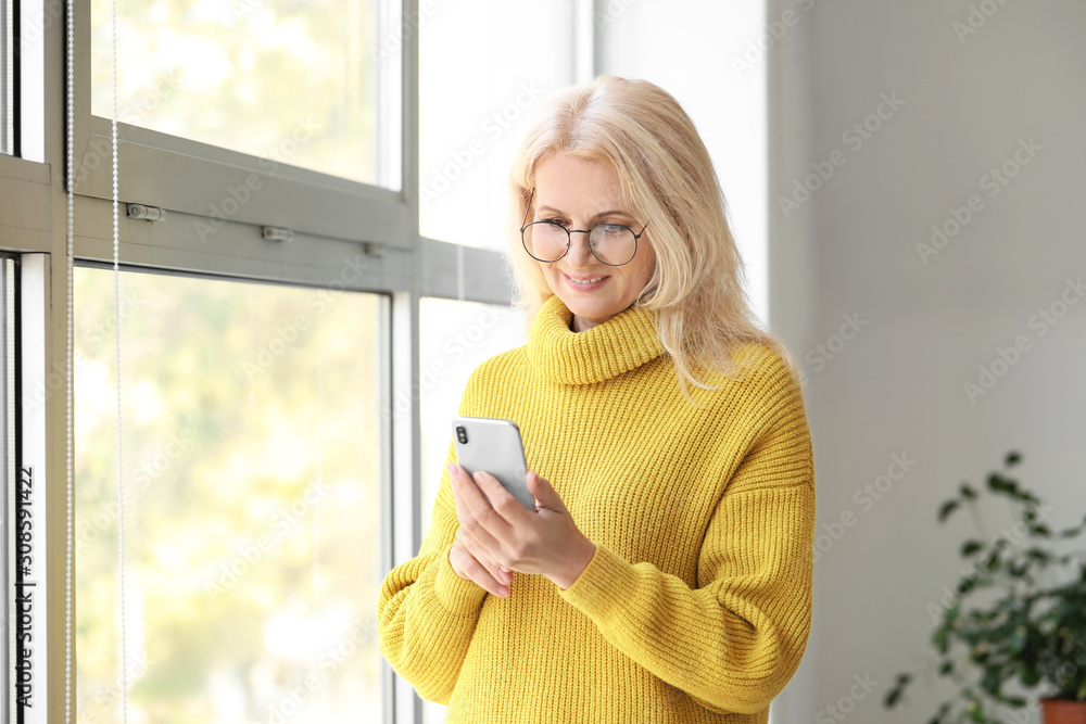 美丽的成熟女人的肖像，靠近窗户拿着手机