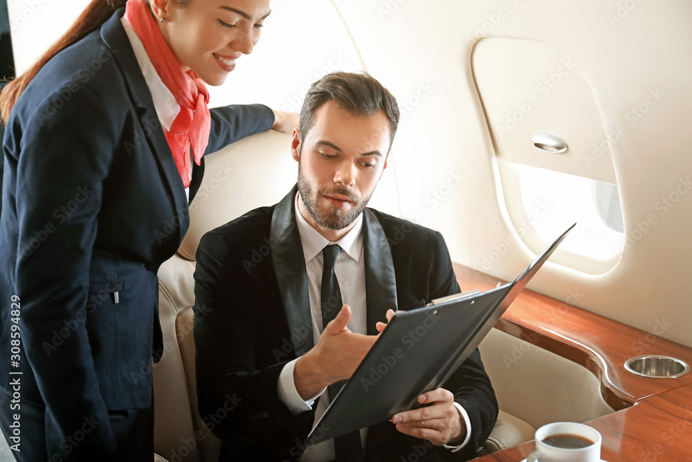 Air hostess showing menu to businessman on board the modern private airplane