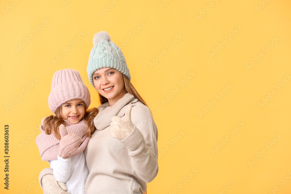 Woman and her little daughter in winter clothes on color background