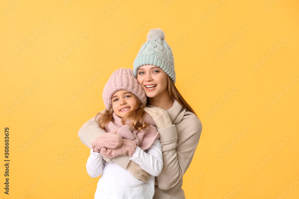 Woman and her little daughter in winter clothes on color background