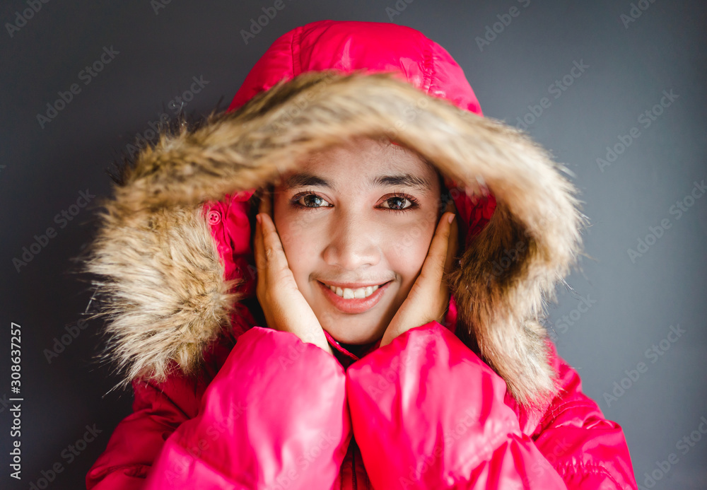 一个穿着冬布的冰冷女人的画像，孤立地站在灰色背景上。微笑的女孩头