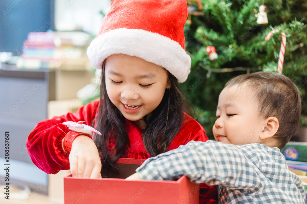 Sibling boy and girl smile and excited and open red gift box on christmas tree background.Childhood 