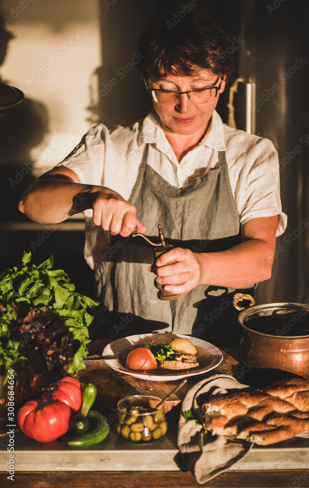 Eldery woman in linen apron putting pepper toTurkish traditional meat soup Haslama with vegetables i