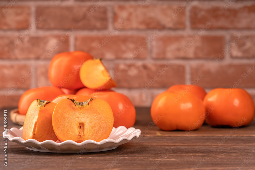 Sliced sweet persimmon kaki in a bamboo sieve basket on dark wooden table with red brick wall backgr