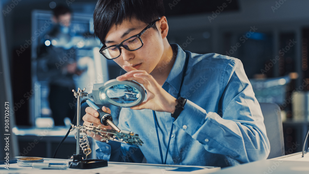 Professional Japanese Electronics Development Engineer in Blue Shirt is Soldering a Circuit Board in