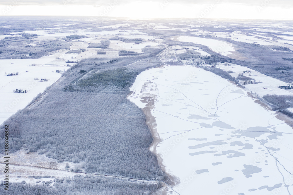 Aerial drone view of a partially frozen lake with unfrozen patches and ice cracks on a winter mornin