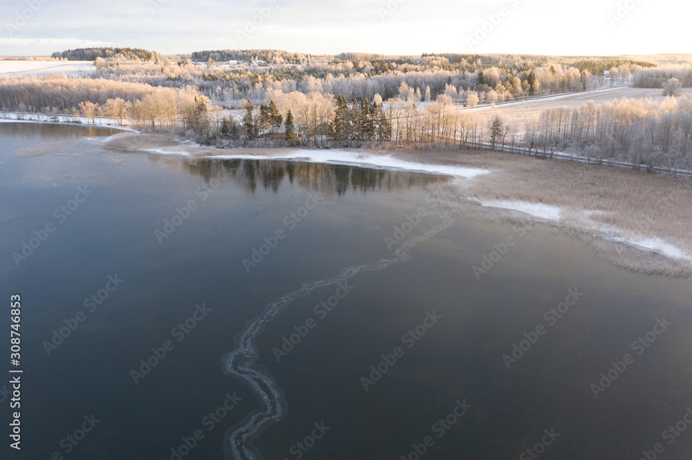 Aerial drone view of a lake coast starting to freeze over in winter sunrise light. Tartu, Estonia.