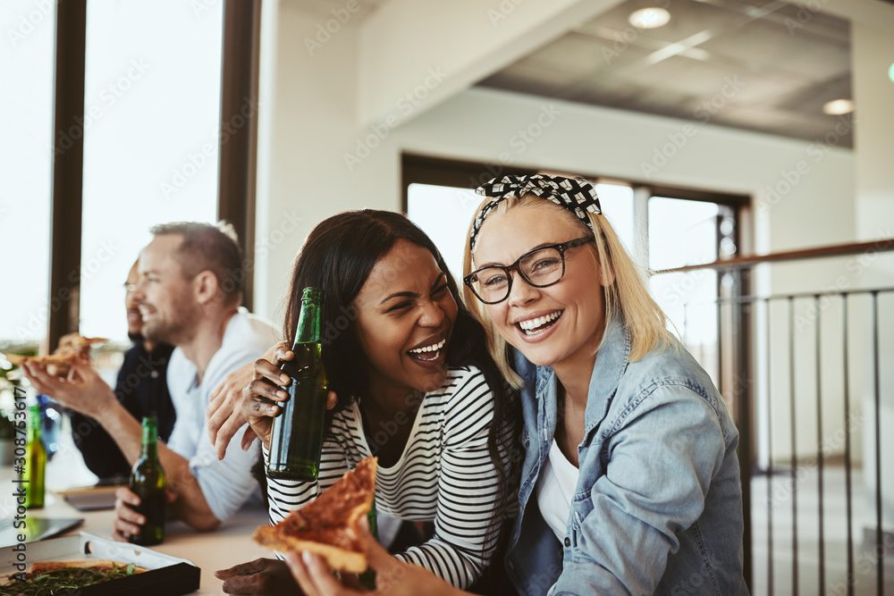 Laughing young businesswomen enjoying pizza and beer after work