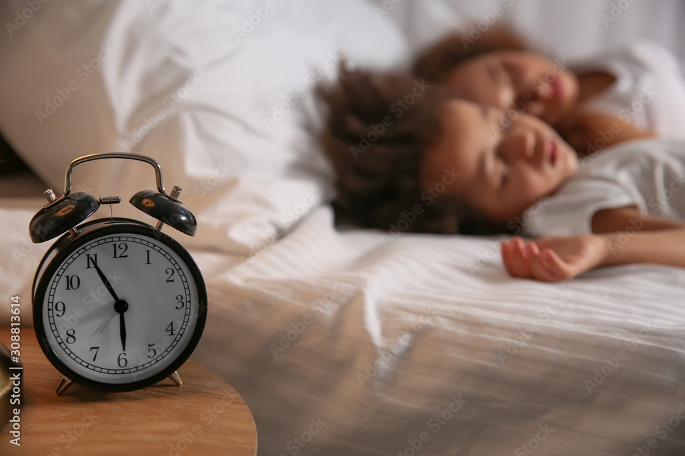 Sleeping African-American girl with mother and alarm clock on table