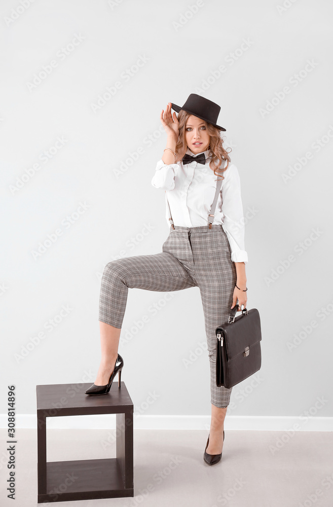 Fashionable young woman against light wall