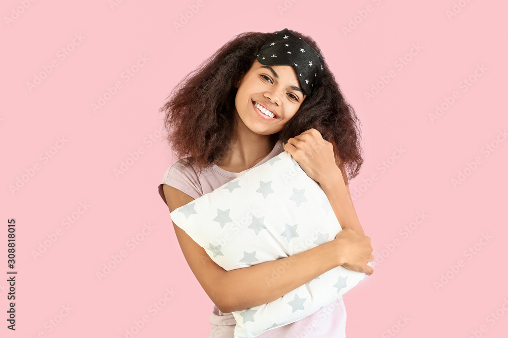 Beautiful African-American woman with sleep mask and pillow on color background