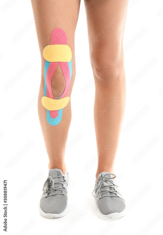 Sporty woman with physio tape applied on knee against white background