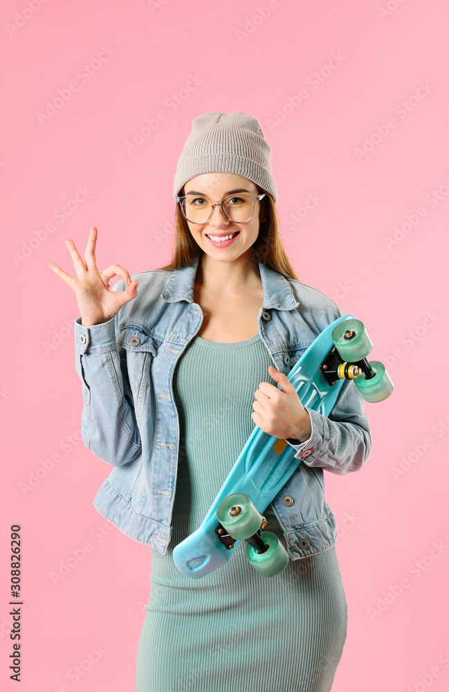 Stylish hipster girl with skateboard showing OK gesture on color background