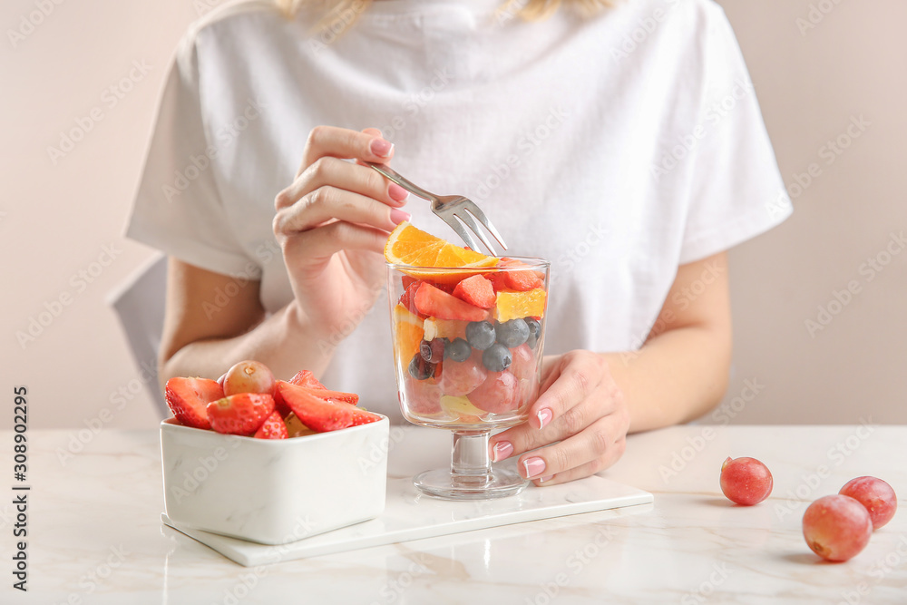 Woman eating tasty fruit salad at table