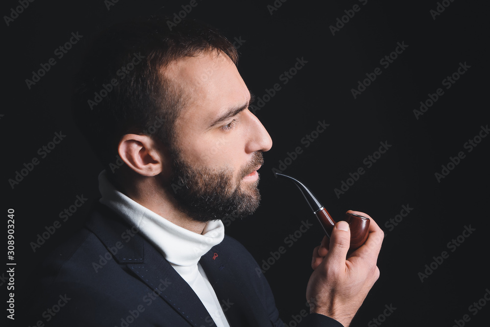 Portrait of stylish young man with smoking pipe on dark background