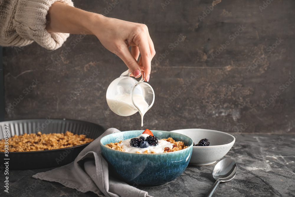 Woman preparing tasty granola with yogurt on grey background