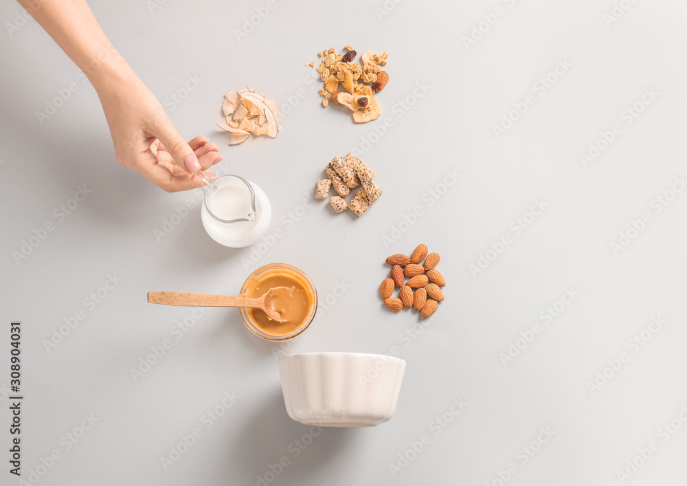 Female hand with jug of yogurt, tasty granola and ingredients on white background