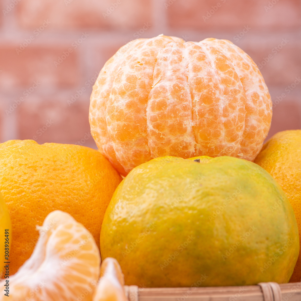 Peeled tangerines in a bamboo sieve basket on dark wooden table with red brick wall background, Chin