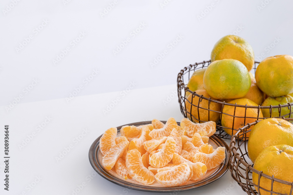 Beautiful peeled tangerines in a plate and metal basket isolated on bright white clean table in a mo