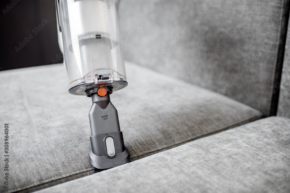 Woman cleaning sofa with a modern cordless vacuum cleaner with a special nozzle, close-up. Dry clean