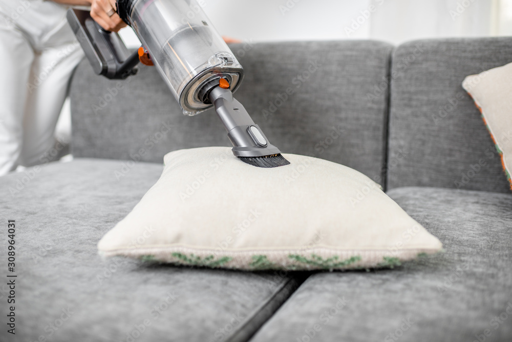 Woman cleaning sofa with a modern cordless vacuum cleaner with a special nozzle, close-up. Dry clean