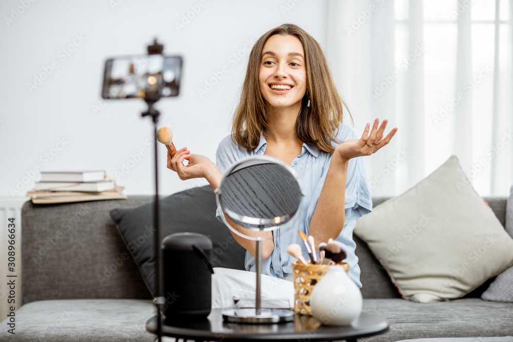 Young woman recording on a smart phone her vlog about cosmetics, showing and demonstrating makeup. I