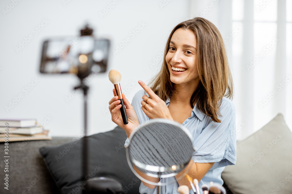 Young woman recording on a smart phone her vlog about cosmetics, showing and demonstrating makeup. I