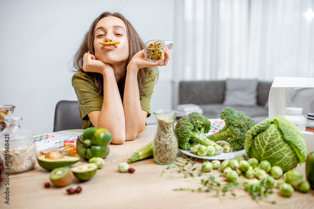 一个年轻快乐的女人的画像，桌上有很多健康的绿色食物。蔬菜的概念