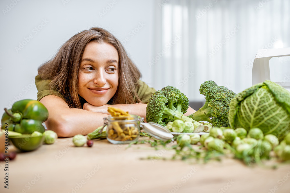 一个年轻快乐的女人的画像，桌上有很多健康的绿色食物。蔬菜的概念