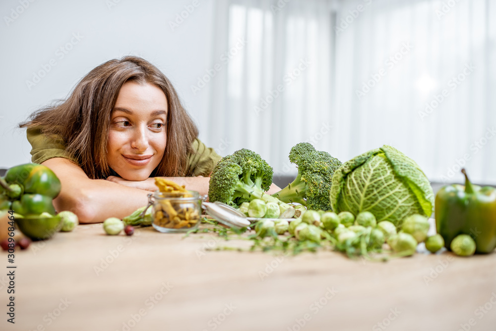 一个年轻快乐的女人的画像，桌上有很多健康的绿色食物。蔬菜的概念