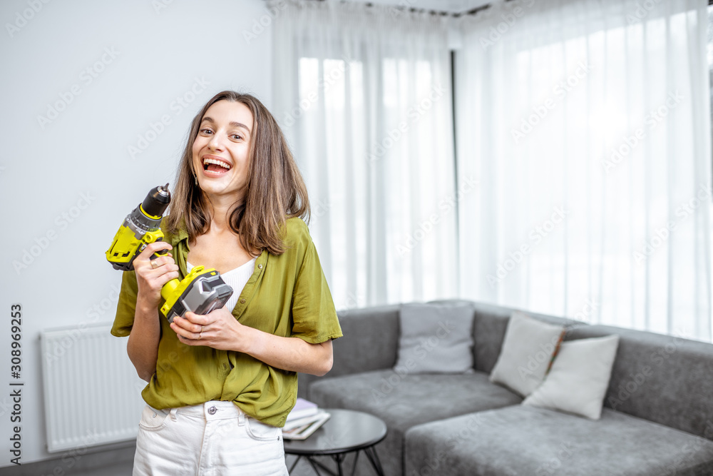 Portrait of a young and happy handywoman with cordless screwdriver at home. Concept of an easy house