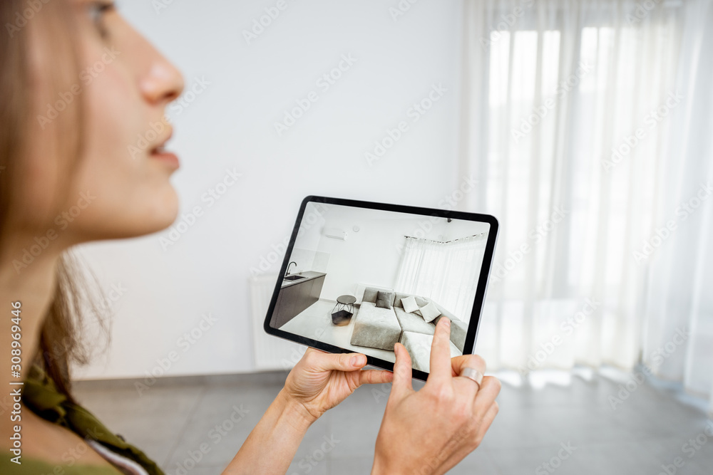 Young woman placing new furniture on a digital tablet into the empty interior, looking how it looks 