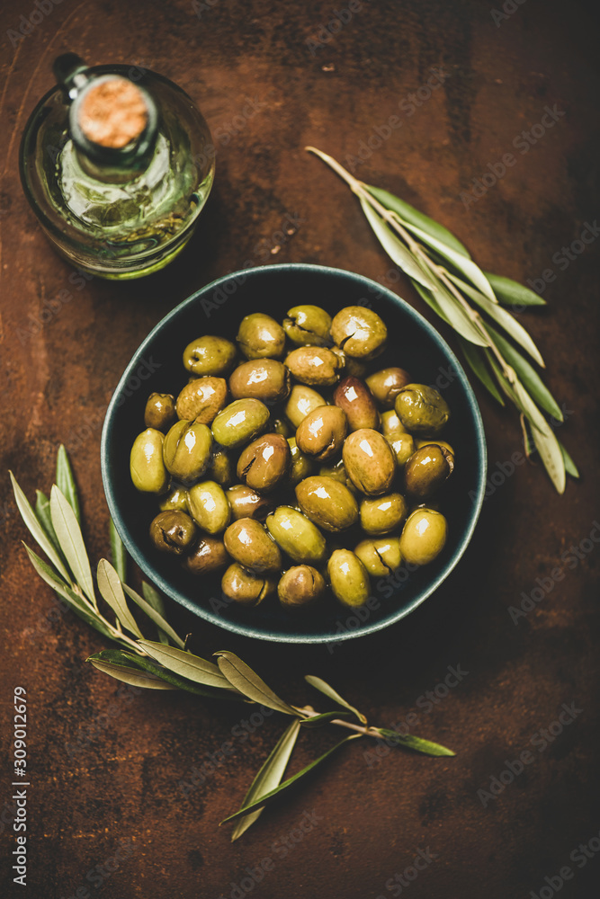 Flat-lay of fresh harvested seasonal pickled green Mediterranean olives in bowl and olive oil in bot